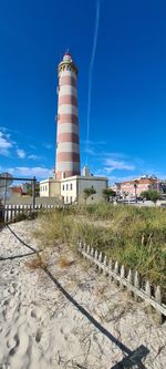 Lighthouse by building against blue sky