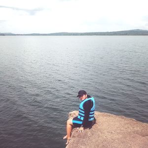 Side view portrait of woman sitting on rock against lake