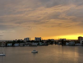 Sea by buildings against sky during sunset