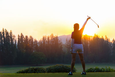 Rear view of woman standing on golf course against sky during sunset