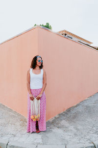 Full length of woman with fruits standing on footpath against wall