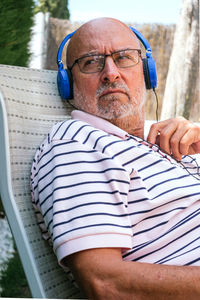 Closeup of a retired senior man looking to the side wearing blue headphones sitting on a lawn chair