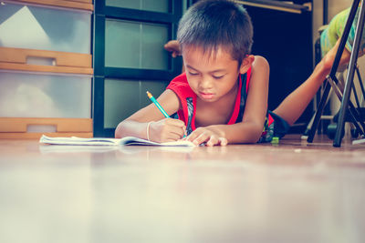 Boy writing in book while lying on floor at home