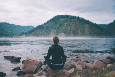 Rear view of man sitting on rock looking at mountains