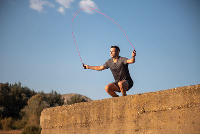 Low angle view of young man jumping against clear sky