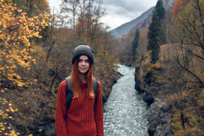 Smiling young woman standing by trees during autumn