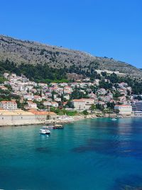 Scenic view of townscape by sea against clear blue sky