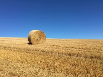 Hay bales on field against clear blue sky