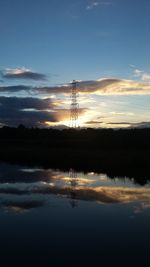 Silhouette electricity pylon by calm lake at sunset