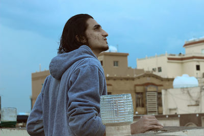 Side view of thoughtful young man looking up while standing on terrace