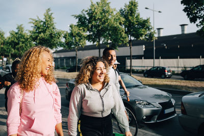 Cheerful friends walking on street by cars in city