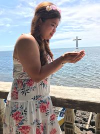 Optical illusion of young woman carrying sunken cemetery cross against sea