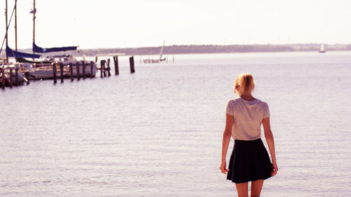 Rear view of woman standing against river on sunny day