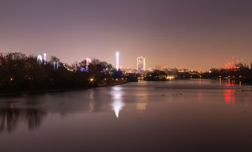 Illuminated buildings by river against sky at night