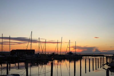 Sailboats moored at harbor against sky during sunset