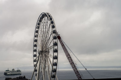 Low angle view of crane and ferris wheel against cloudy sky