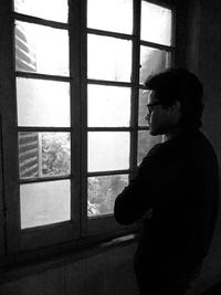 Side view of young man looking through window at home