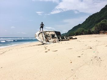 Man standing on shipwreck at beach against sky