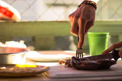 Cropped hands of man cutting meat on cutting board