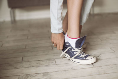 Low section of girl putting on canvas shoe at home
