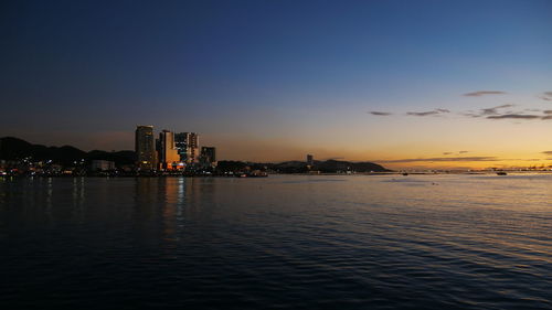 Sea by illuminated buildings against sky during sunset