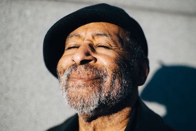 Smiling senior man with eyes closed against wall