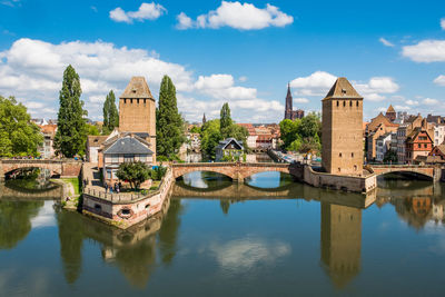 Arch bridge over river by buildings against sky in city