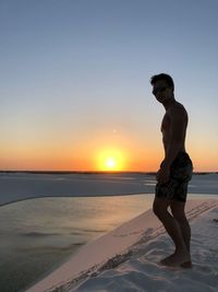 Man standing at beach against sky during sunset