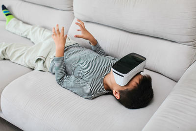 Boy wearing virtual reality simulator while lying on sofa in home