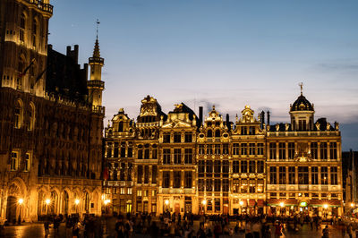 Crowd at illuminated building in city against sky at dusk