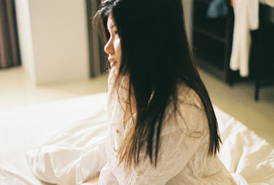 Side view of thoughtful young woman sitting on bed at home