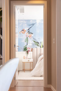 Interior of bedroom with floral ornament on wall with comfortable bed under blanket placed near round bedside table with vase of fresh plants