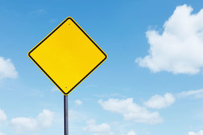 Low angle view of blank yellow road sign against sky