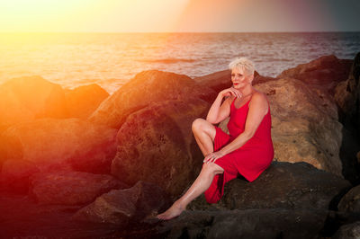 Woman sitting on rock at beach during sunset