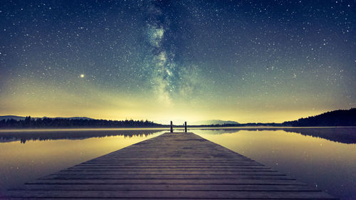 Pier over lake against sky at night