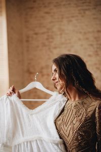 Woman holding wedding dress while standing against wall