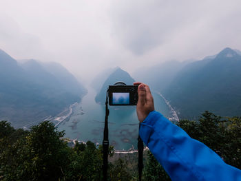 Man photographing using mobile phone against sky