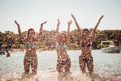 Female friends splashing water in sea during sunset