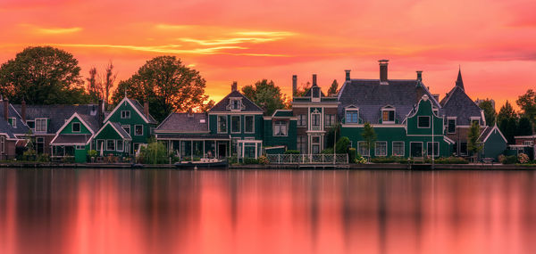 Scenic view of river by buildings against orange sky