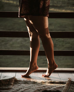 Lower section of woman on ledge of wooden cabin at sunset