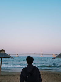 Rear view of man looking at sea against clear sky