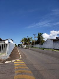 Empty road by buildings against blue sky