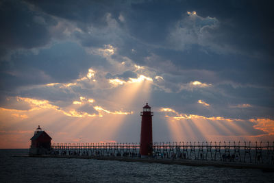 Lighthouse by sea against sky during sunset