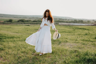 Full length of beautiful woman with sun hat walking on grassy land