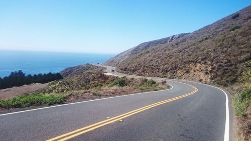 Road by mountain and sea against clear sky