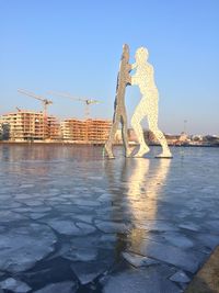 Statue by sea against clear blue sky