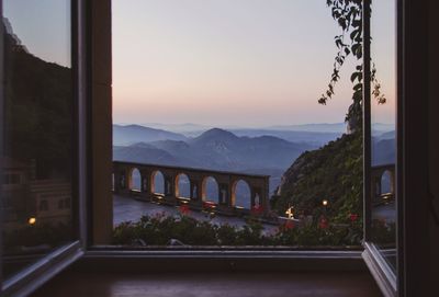 Bridge by mountains against sky during sunset seen through window