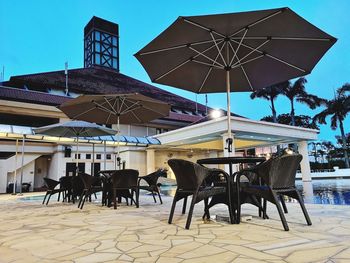 Chairs and tables at sidewalk cafe in city against sky