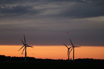 Silhouette wind turbines on field against sky during sunset