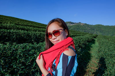 Side view portrait of young woman wearing sunglasses standing on field against clear sky during sunny day